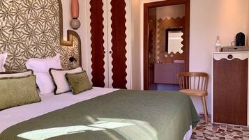 A bedroom with a large bed, a wooden wardrobe, a chair, and a bathroom visible through a door.