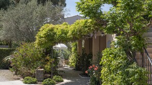 Un sentier de jardin qui mène à un bâtiment surmonté d’une pergola recouverte de verdure.