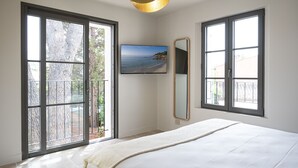 Une chambre avec un grand lit, un téléviseur fixé au mur et une vue sur la mer par les fenêtres.