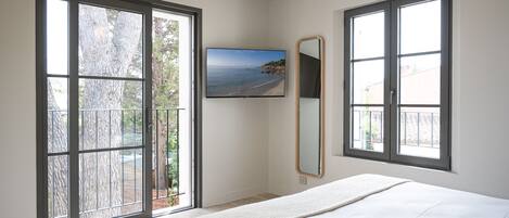 A bedroom with a large bed, a TV mounted on the wall, and a view of the sea through the windows.