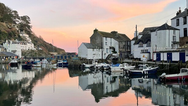 A harbor with boats docked, buildings along the waterfront, and a calm water surface reflecting the structures. - Stunning Views of Polperro Harbour from this Waterfront Cottage. Free Parking. (Polperro)