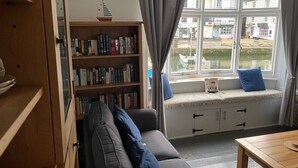 A cozy living room with a sofa, a bookshelf, a window seat, and a view of the outside. - Stunning Views of Polperro Harbour from this Waterfront Cottage. Free Parking. (Polperro)