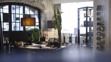 A modern office space with a desk, computer, and various office supplies. There is a large window with a view of the city, and a bookshelf filled with books and decorative items.