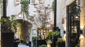 A courtyard with two round tables, potted plants, and a stone floor. - Petit Hôtel Confidentiel (Chambery)
