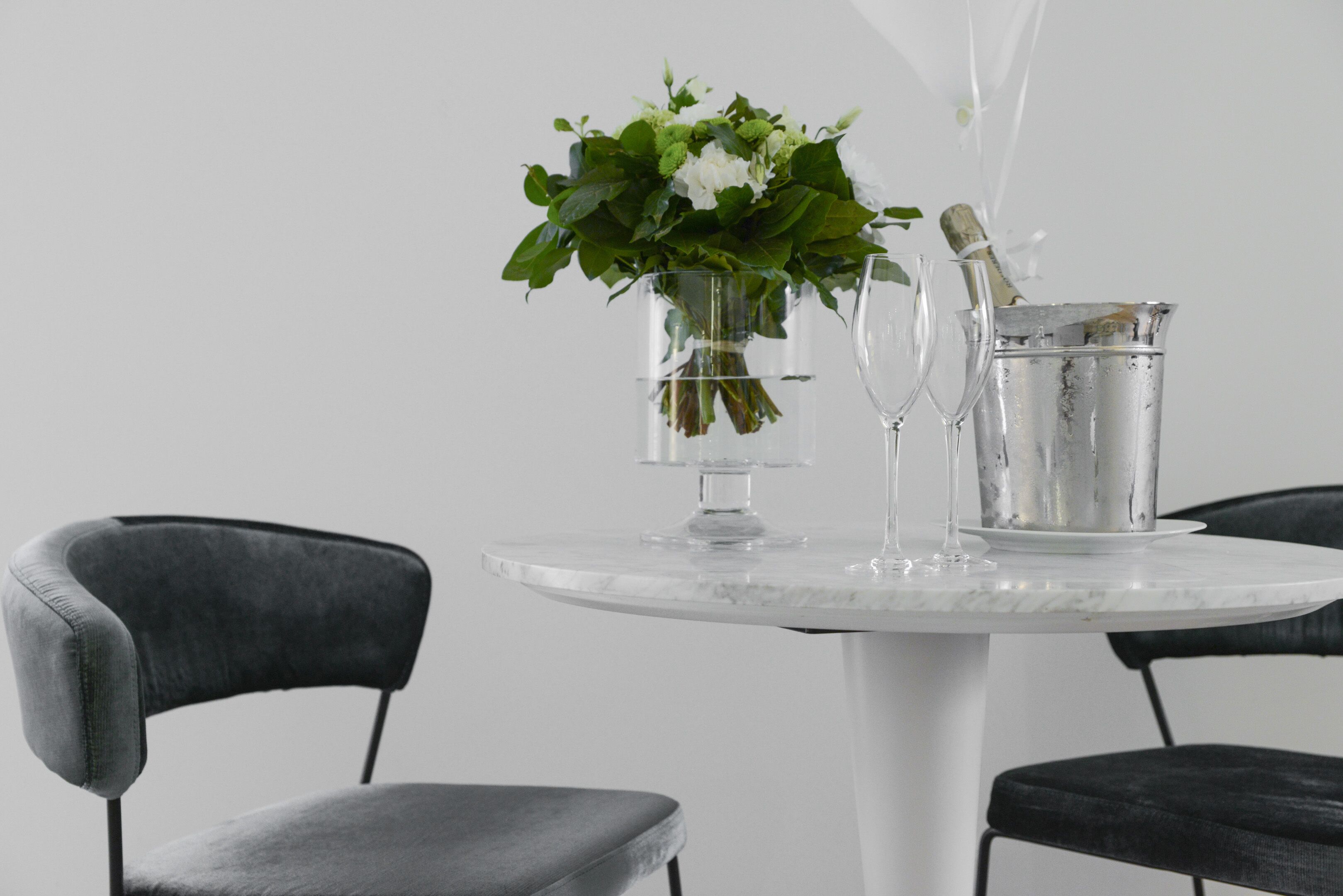 A table with a vase of flowers, a champagne bottle, and two wine glasses.