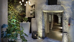 A stone-walled interior with a staircase leading to an upper level, surrounded by indoor plants and modern lighting fixtures. - Petit Hôtel Confidentiel (Chambery)