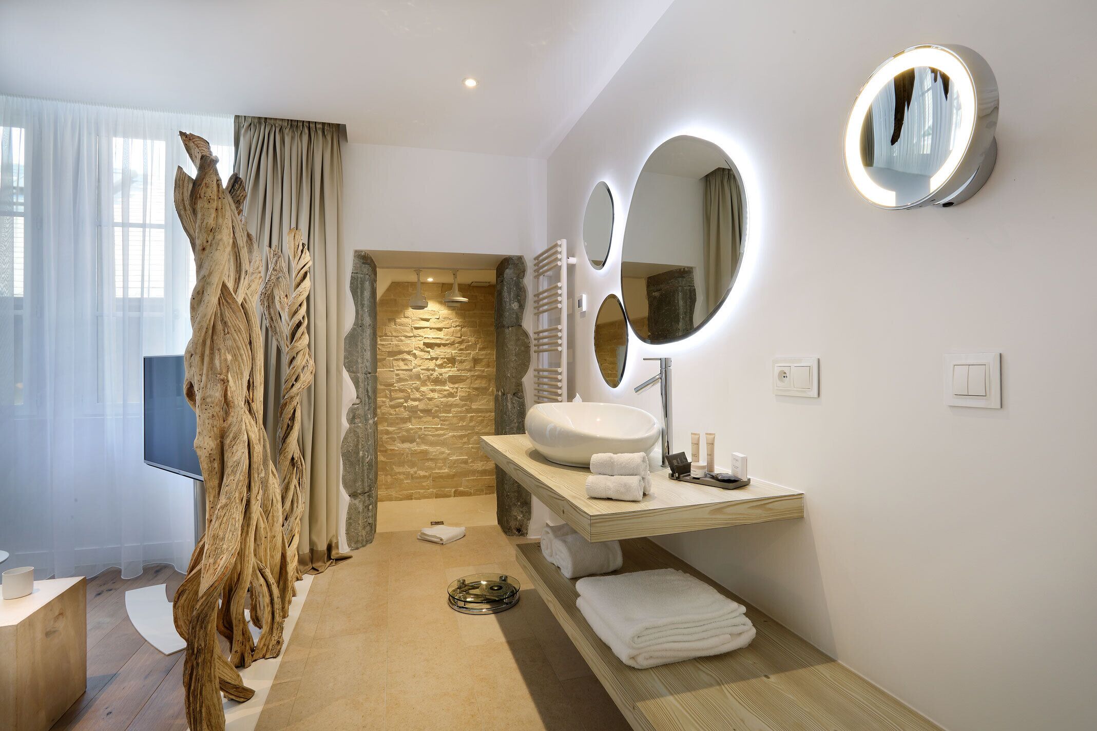 Un baño moderno con pared de piedra, tocador de madera y un espejo grande con iluminación integrada.