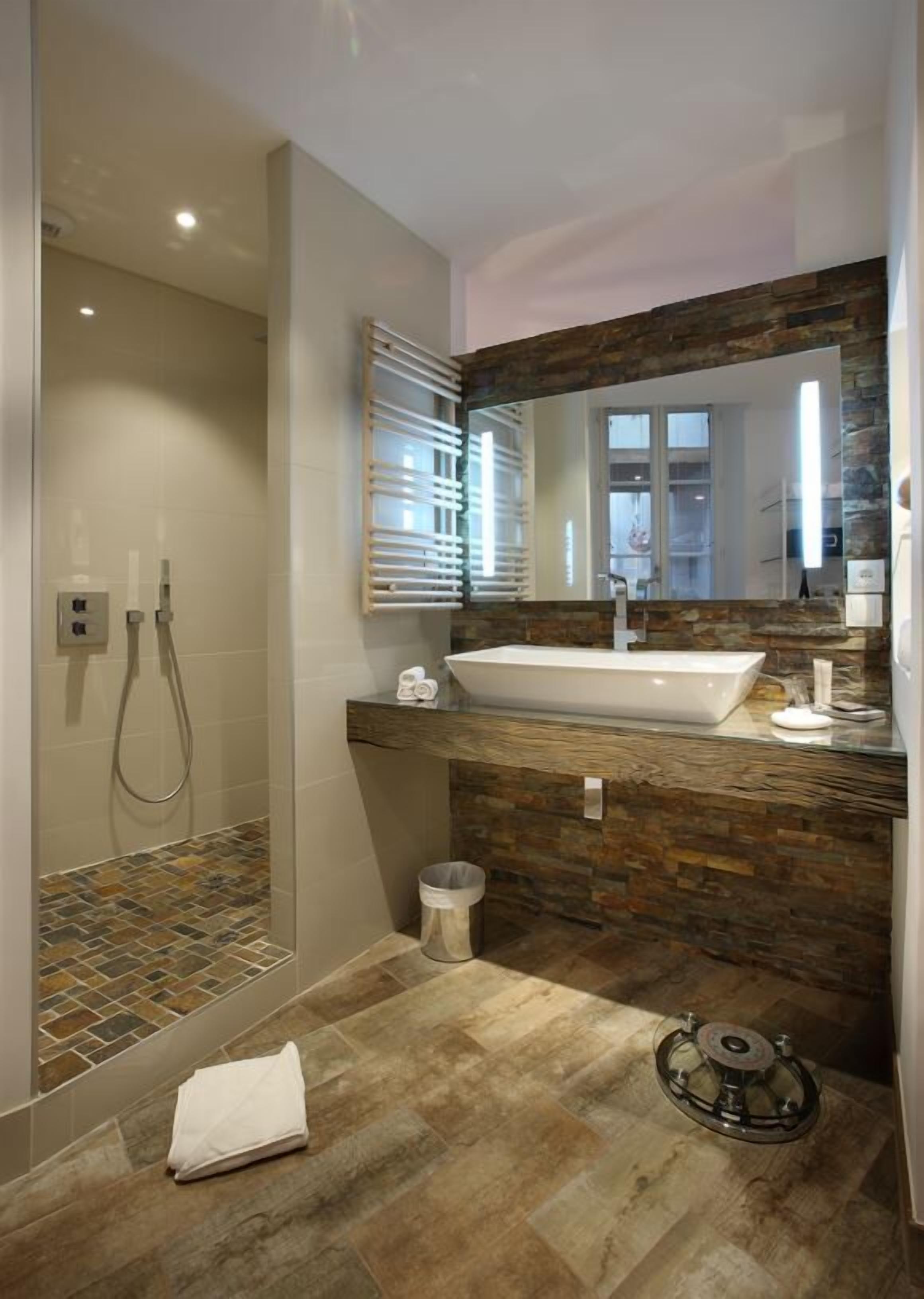 A modern bathroom with a glass-enclosed shower, a large mirror, and a stone-textured countertop.