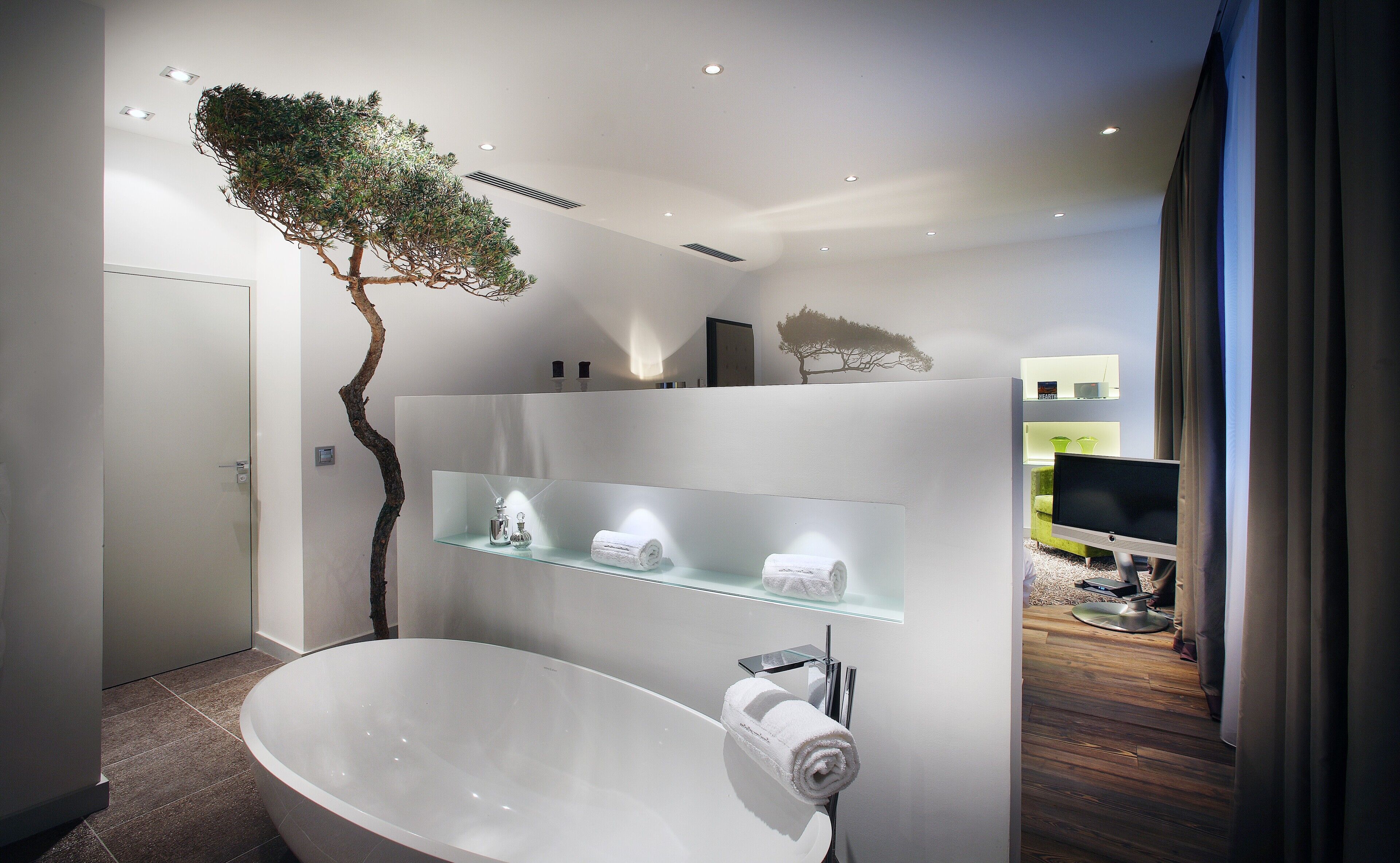 A modern bathroom with a freestanding bathtub, a glass shelf with toiletries, and a tree sculpture.