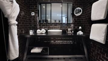 Un baño moderno con paredes de azulejos negros, un espejo grande, un lavabo redondo y toallas ordenadamente dobladas.