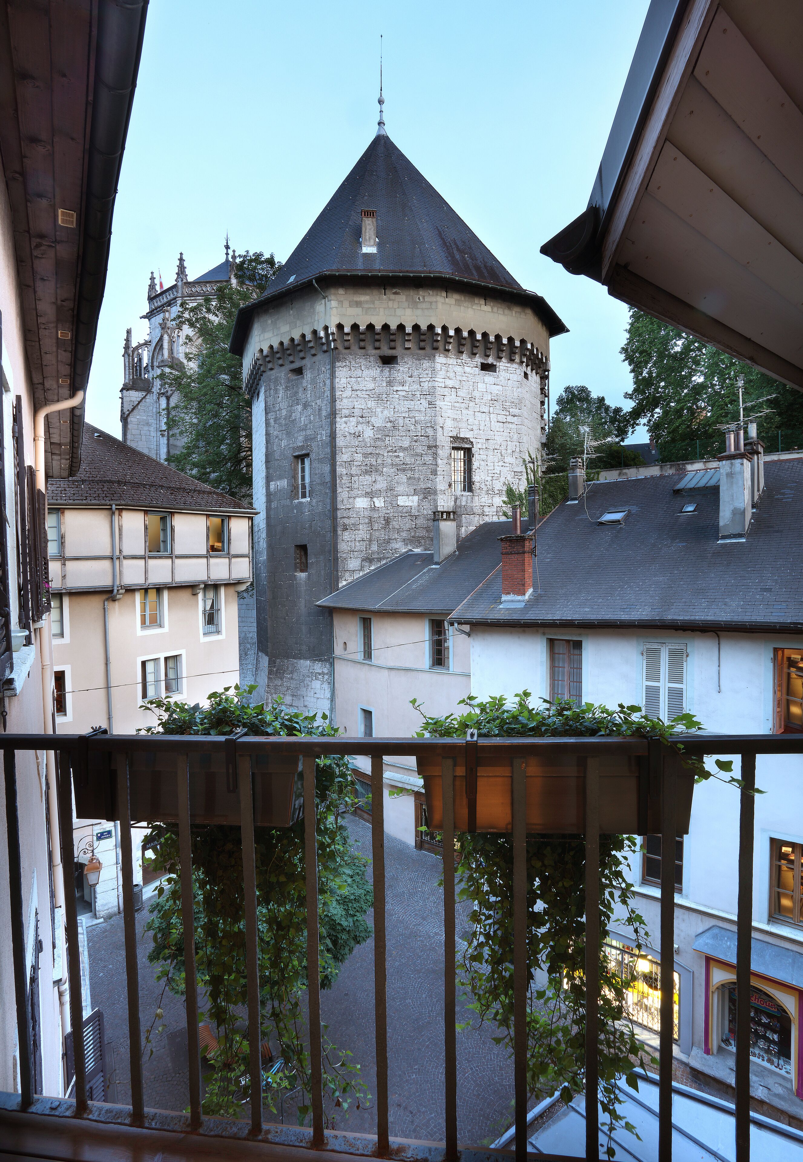 Ein Blick auf einen Turm mit einem Zinnenturm, umgeben von Gebäuden mit Balkonen und einer Straße darunter.