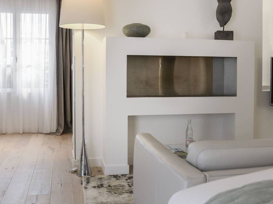 A modern bedroom with a bed, bedside table, lamp, and a wall-mounted shelf with decorative items.