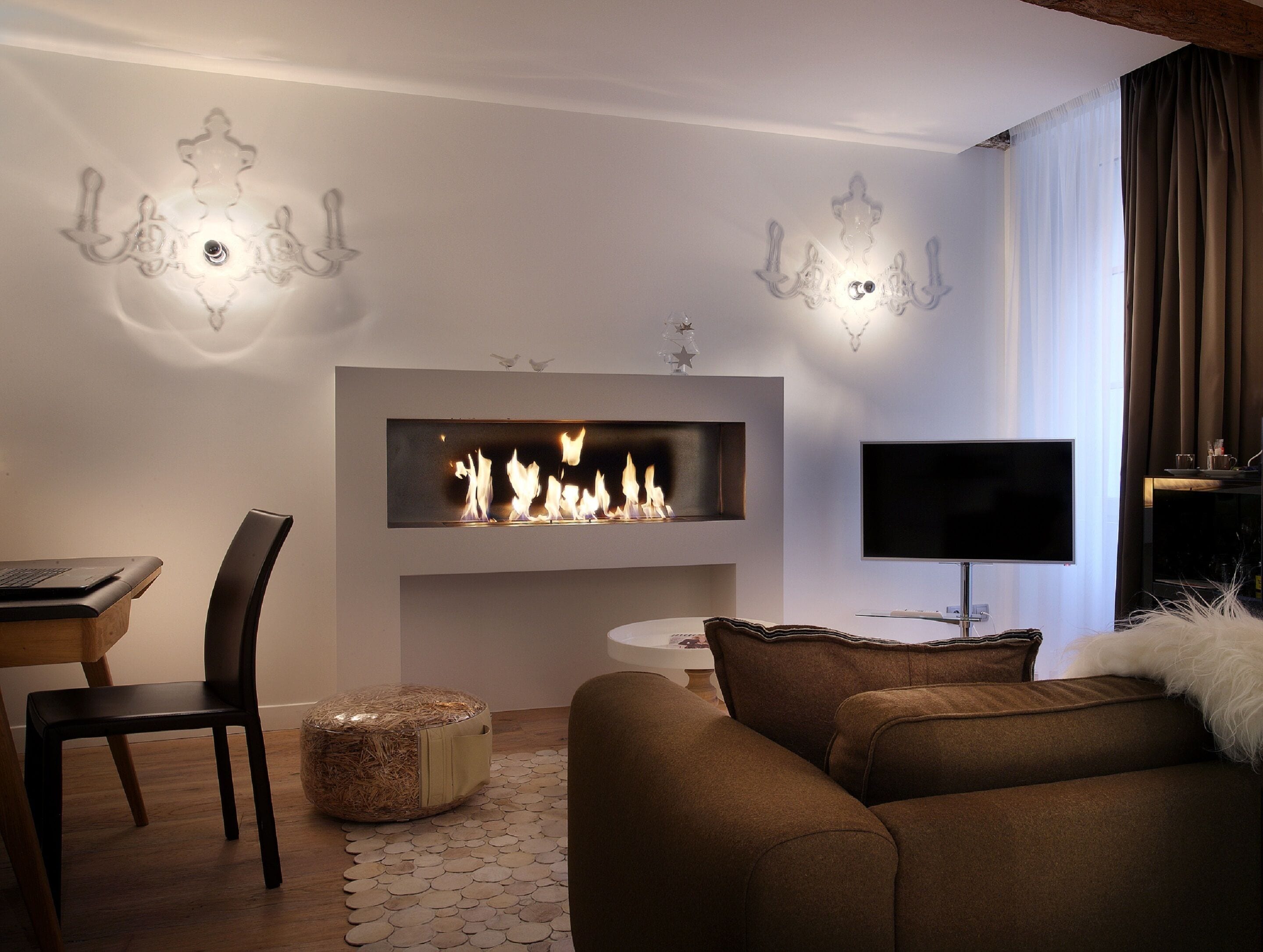 Una sala de estar moderna con chimenea, un televisor de pantalla plana, una computadora portátil sobre una mesa de madera y un sofá marrón.