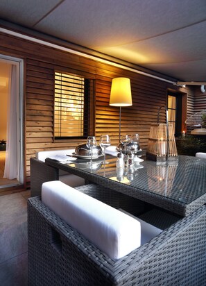 Un área de comedor al aire libre con mobiliario de mimbre, una mesa de vidrio y una lámpara.