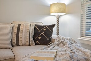 Ein gemütliches Schlafzimmer mit Bett, Kissen, Decke, Lampe und einem Fenster mit Jalousien.
