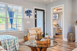 Un salon avec une table basse en verre, un canapé et un fauteuil. Il y a une porte ornée d’une étoile de mer sur le mur.