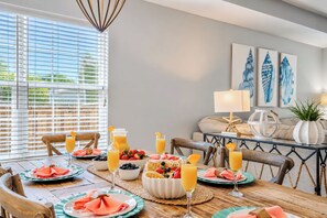 Un coin repas avec une table en bois mise pour le petit-déjeuner, comprenant des assiettes, des verres et un saladier de fruits.
