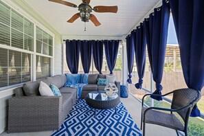 Eine überdachte Veranda mit einer grauen Couch, einem blau gemusterten Teppich und Korbstühlen.