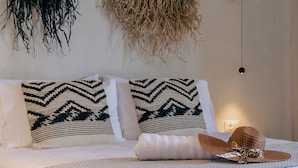 A bed with patterned pillows, a woven hat, and a hanging plant.