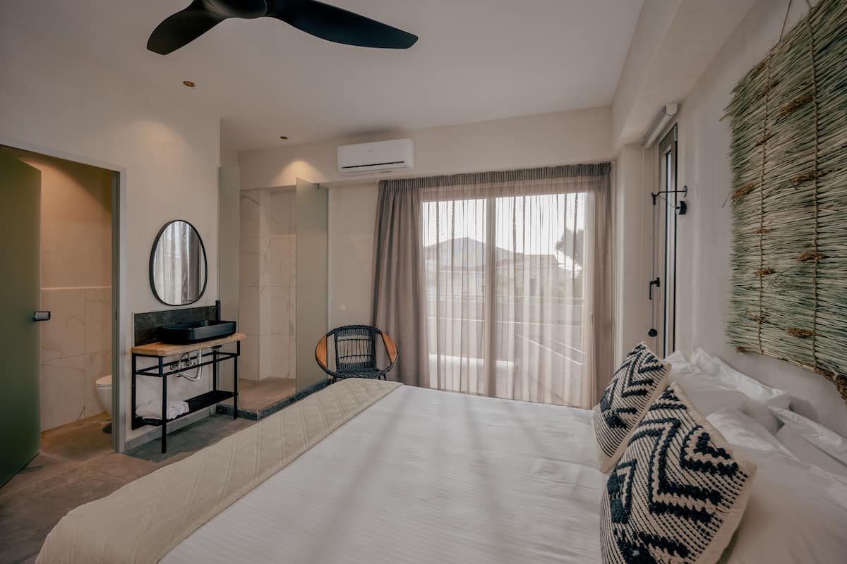 Una habitación de hotel con cama, tocador con espejo, una silla y ventana con cortinas.