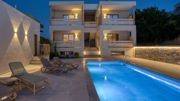 A modern two-story building with a swimming pool, outdoor seating, and a stone wall.