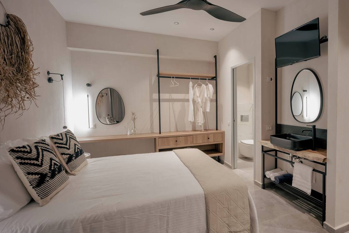 Un dormitorio moderno con cama, mesitas de noche, espejo, armario y baño con lavabo y espejo.