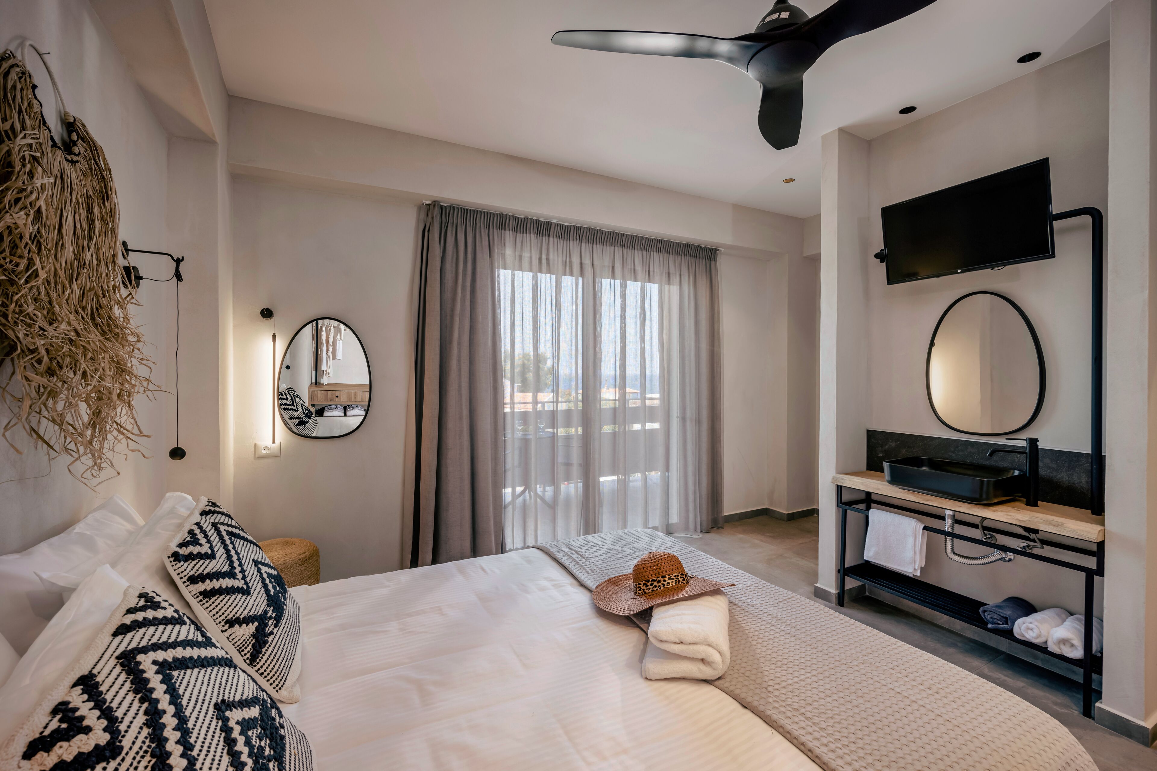 Een moderne hotelkamer met een bed, een kaptafel met spiegel, een flatscreen televisie en een plafondventilator.
