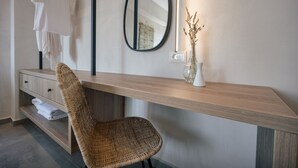 A modern bathroom with a wooden vanity, a wicker chair, a mirror, and a vase with dried flowers.