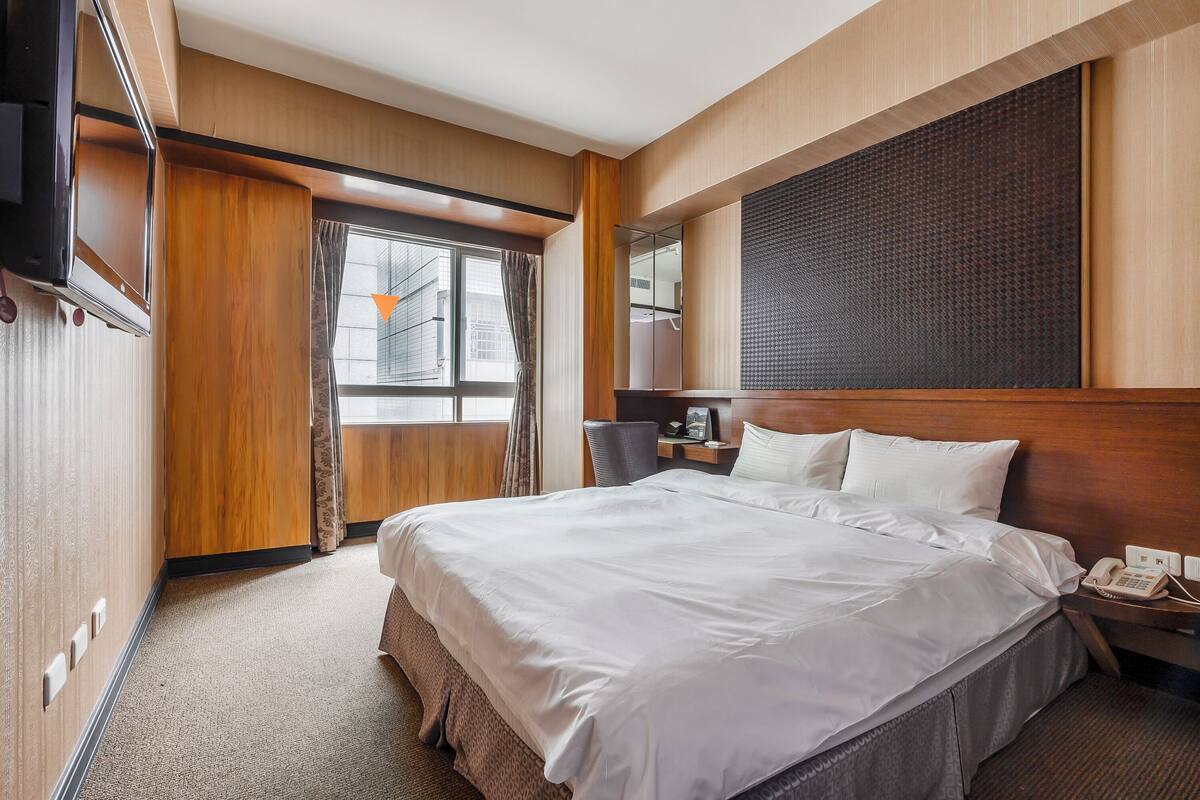 A hotel room with a large bed, a desk with a telephone, and a window with curtains.