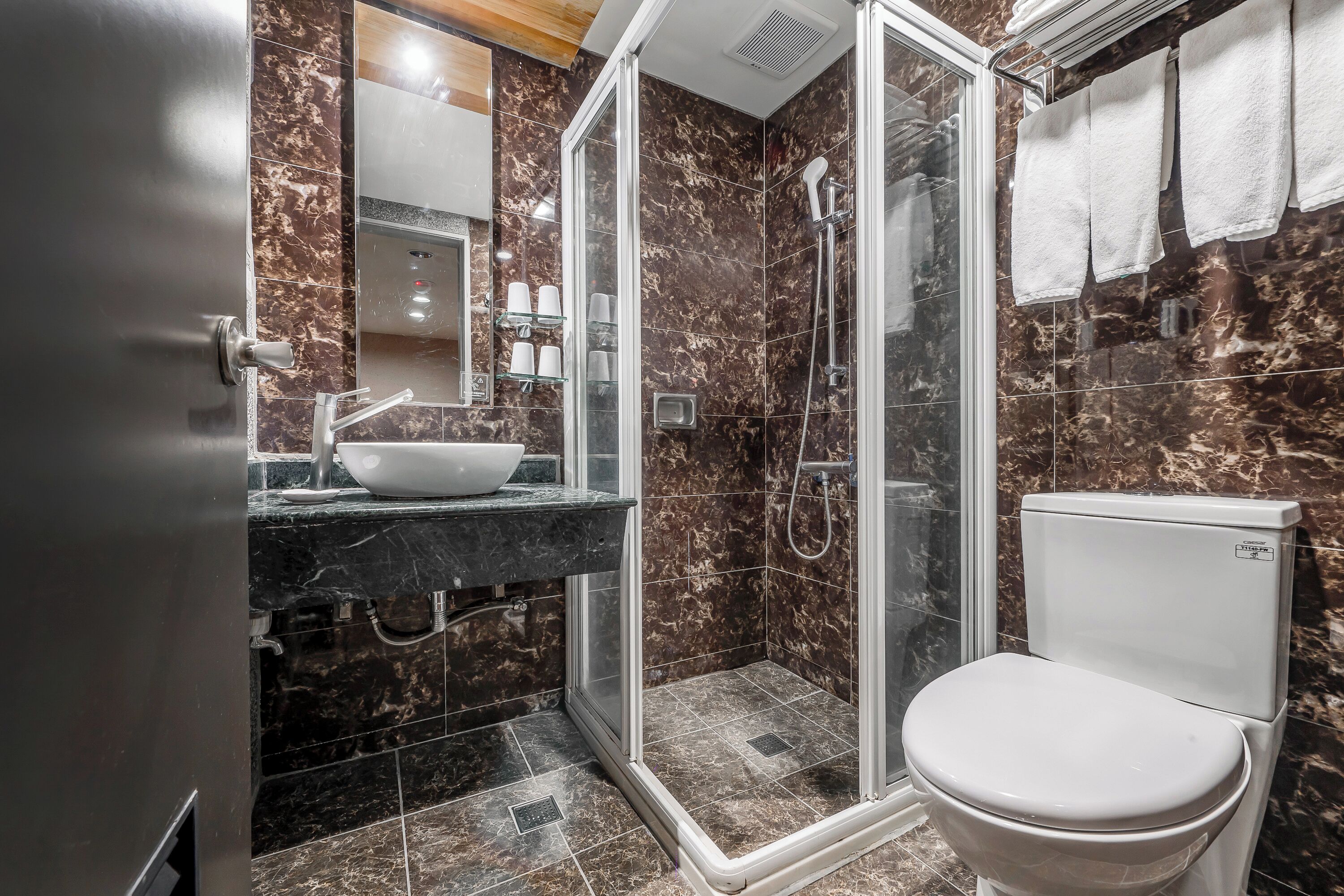 Un baño moderno con ducha envuelta en vidrio, inodoro blanco y zona de lavamanos con azulejos de mármol.