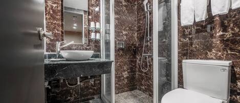 Un baño moderno con ducha envuelta en vidrio, inodoro blanco y zona de lavamanos con azulejos de mármol.