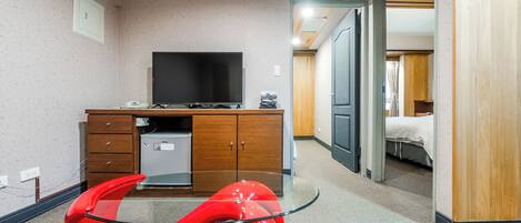 A hotel room with a glass-top desk, a red chair, a television, a wardrobe, and a bed.