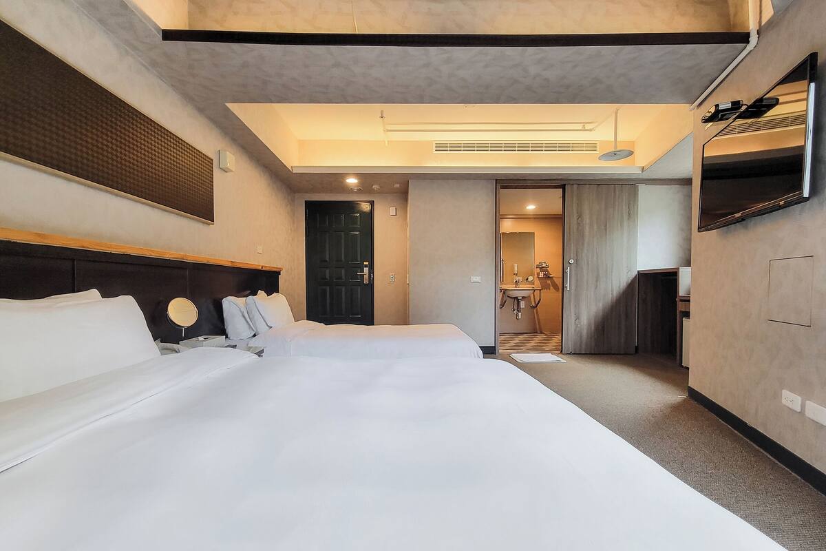 A hotel room with a large bed, a TV, and a bathroom visible through an open door.