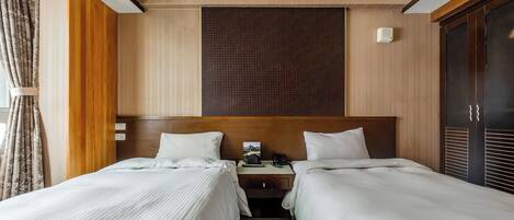 Habitación de hotel con dos camas, cabecera de madera, mesita de noche con teléfono y una ventana grande con cortinas.