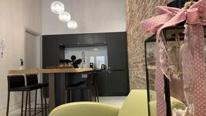 A modern kitchen with dark cabinets, a wooden countertop, and a hanging light fixture. There are two chairs and a table in the foreground. - At the Well of Light Suites Sandolo: double/single bedroom w/private bath. (Venezia)