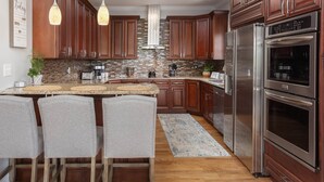 A modern kitchen with dark wood cabinets, stainless steel appliances, and a central island with bar stools. - Mountain Views, Hot Tub, Game Room | 20 min to Asheville! One Mile to Mars Hill University! (Mars Hill)