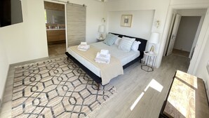 A modern bedroom with a large bed, bedside lamps, a patterned rug, and a view of the bathroom. - 5 bedroom villa with sea view in Tourettes (Tourrettes-sur-Loup)
