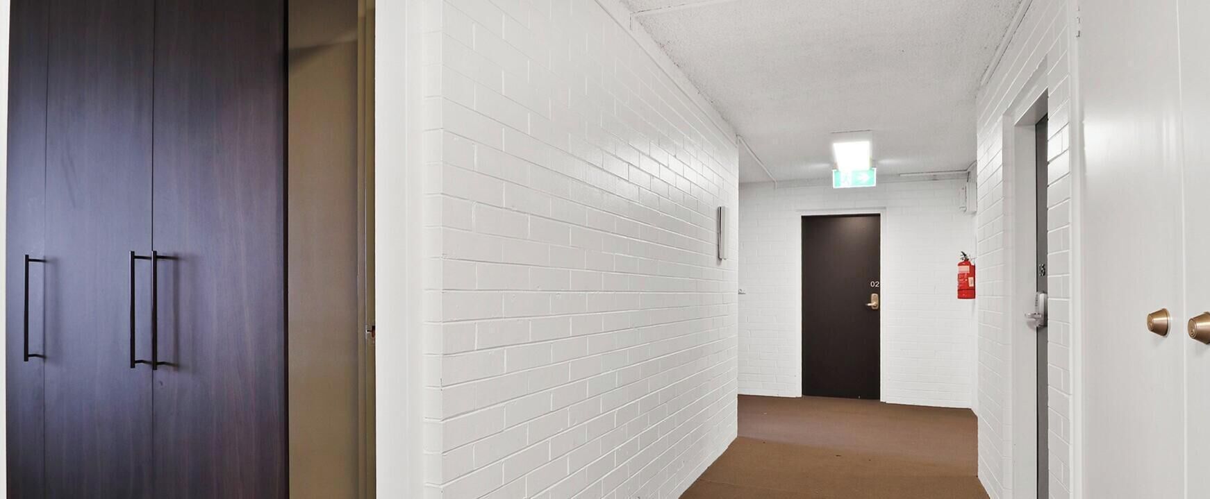 En hall med vita tegelväggar, en brun matta och en mörk trädörr med texten ”Skidförråd”.