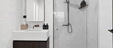 A modern bathroom with a white sink, dark wood cabinet, and a glass shower enclosure.