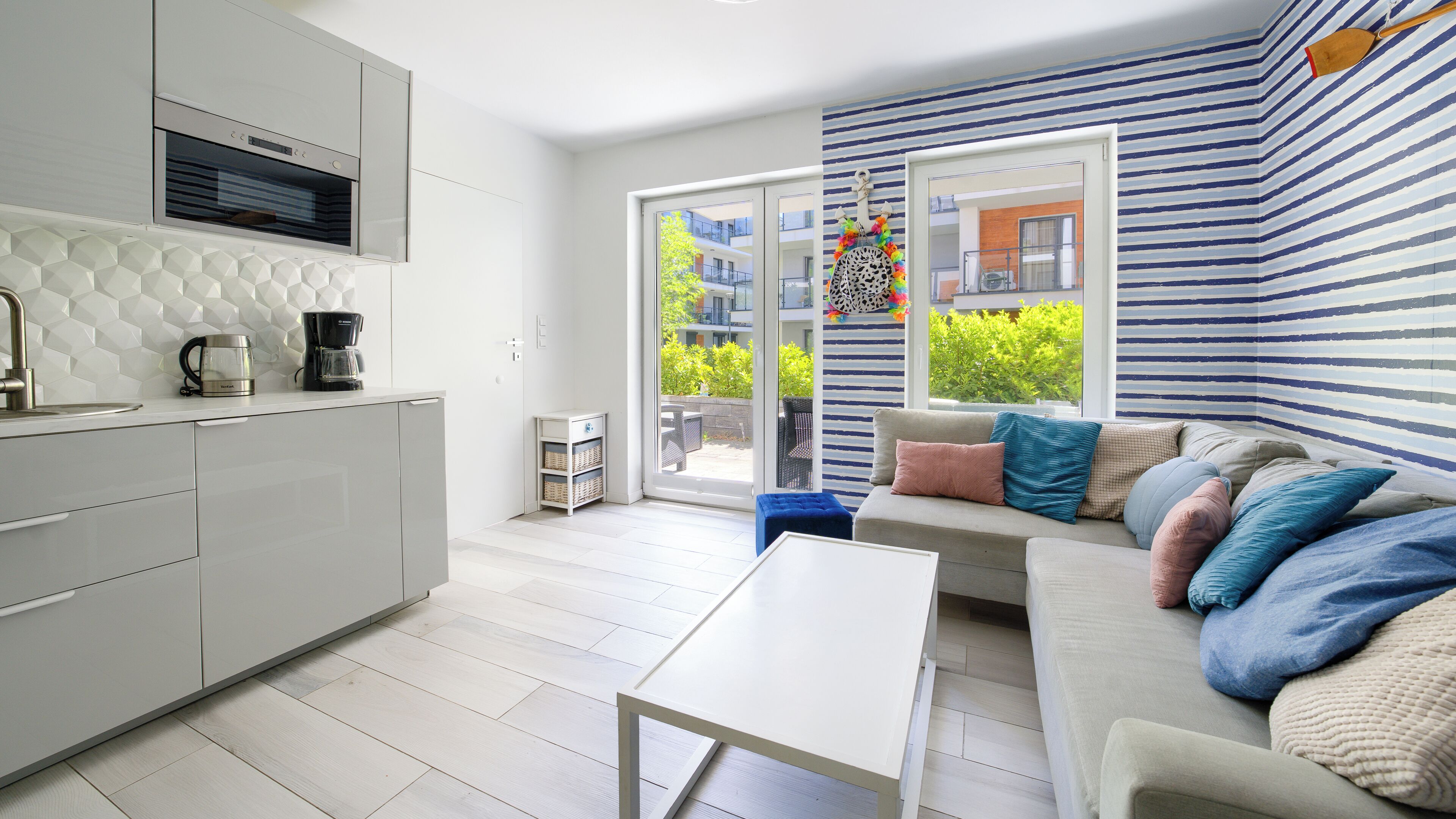 A modern kitchen with a coffee maker, a dining area with a white table, and a sofa with multiple cushions.