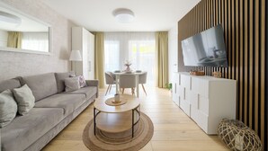 A modern living room with a sofa, a dining table, and a TV. - Apartamenty Sun & Snow Baltic Apartments (Pobierowo)