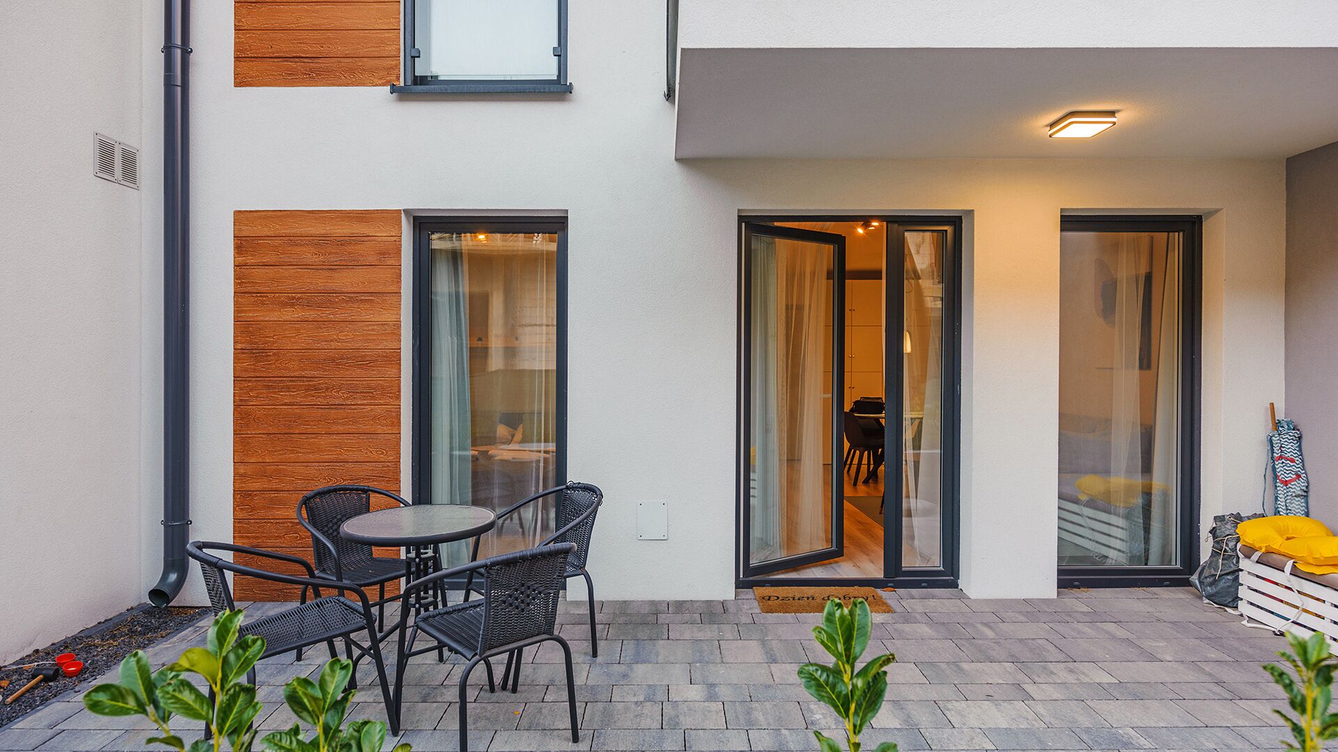 A modern outdoor seating area with a table and chairs, a wooden accent wall, and a glass door leading to an interior space.
