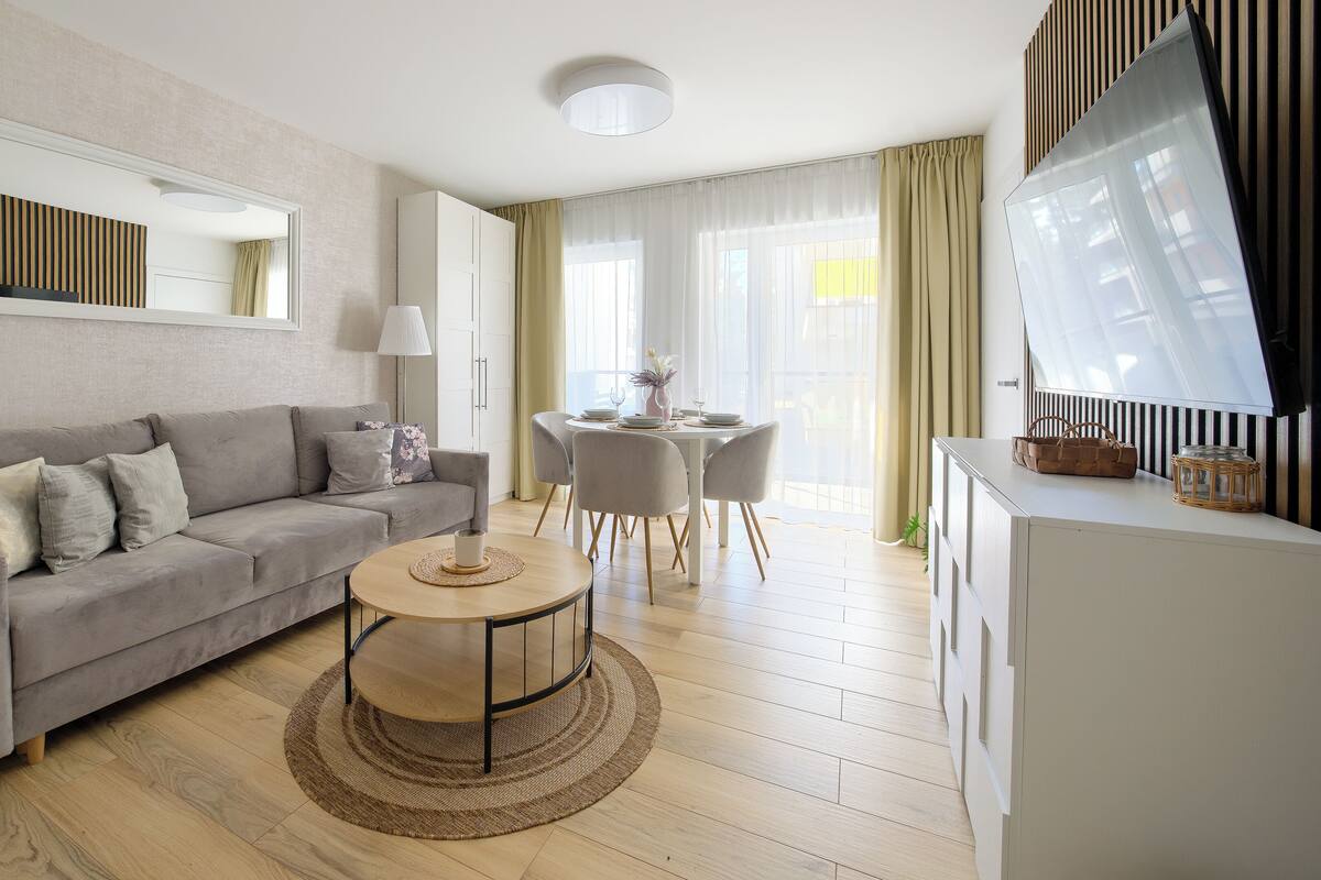 Un salon moderne avec un canapé gris, une table basse ronde et un coin repas comprenant une table et des chaises blanches.