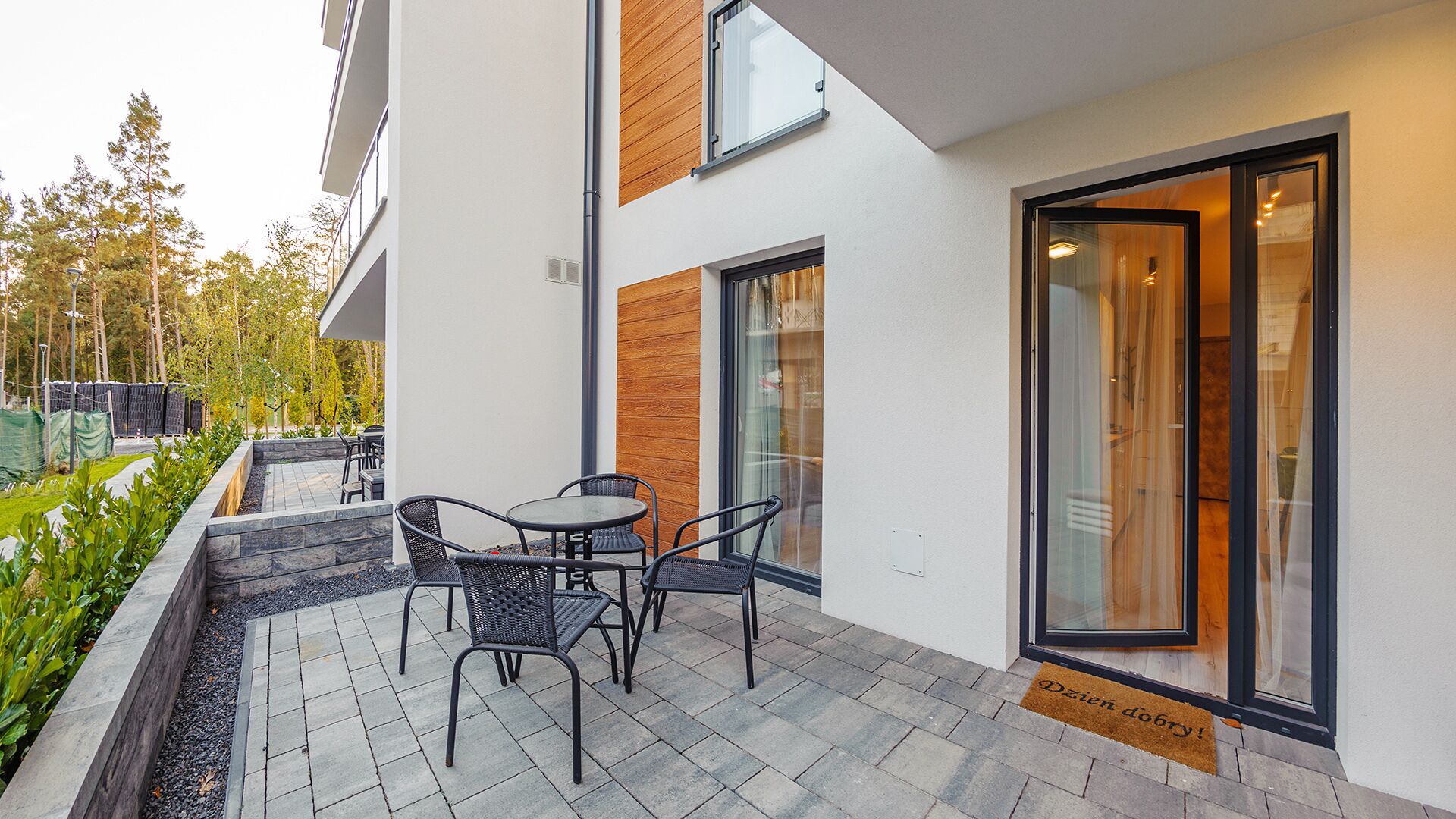 Un espacio moderno al aire libre con una mesa, sillas, un muro decorativo de madera y una entrada con puerta de vidrio.