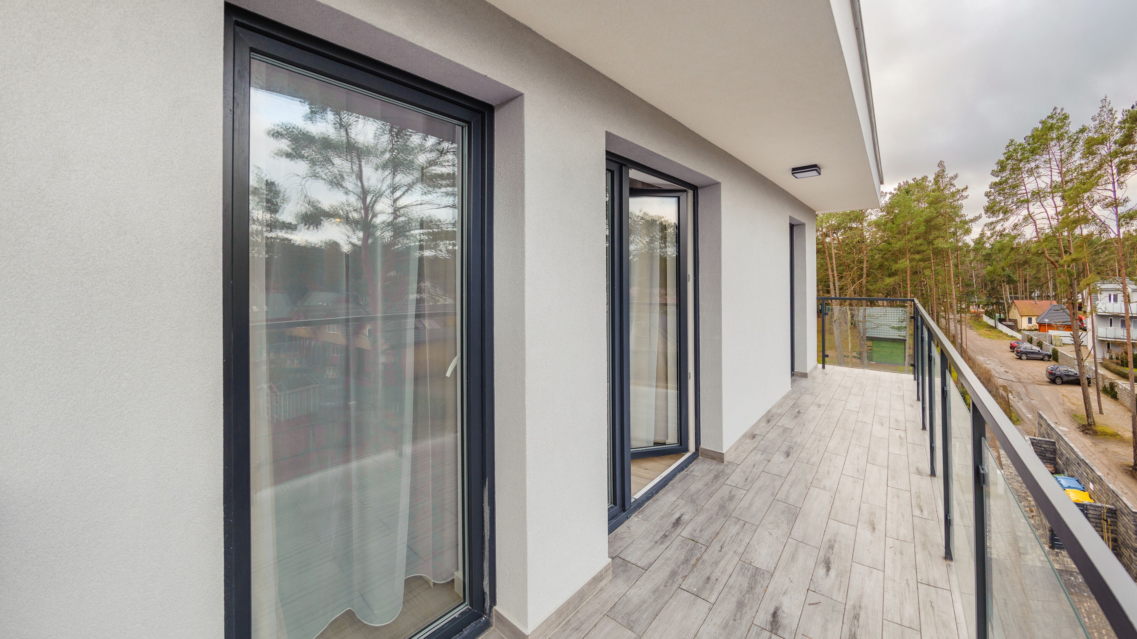 A balcony with large windows, a view of the street, and a wooden floor.