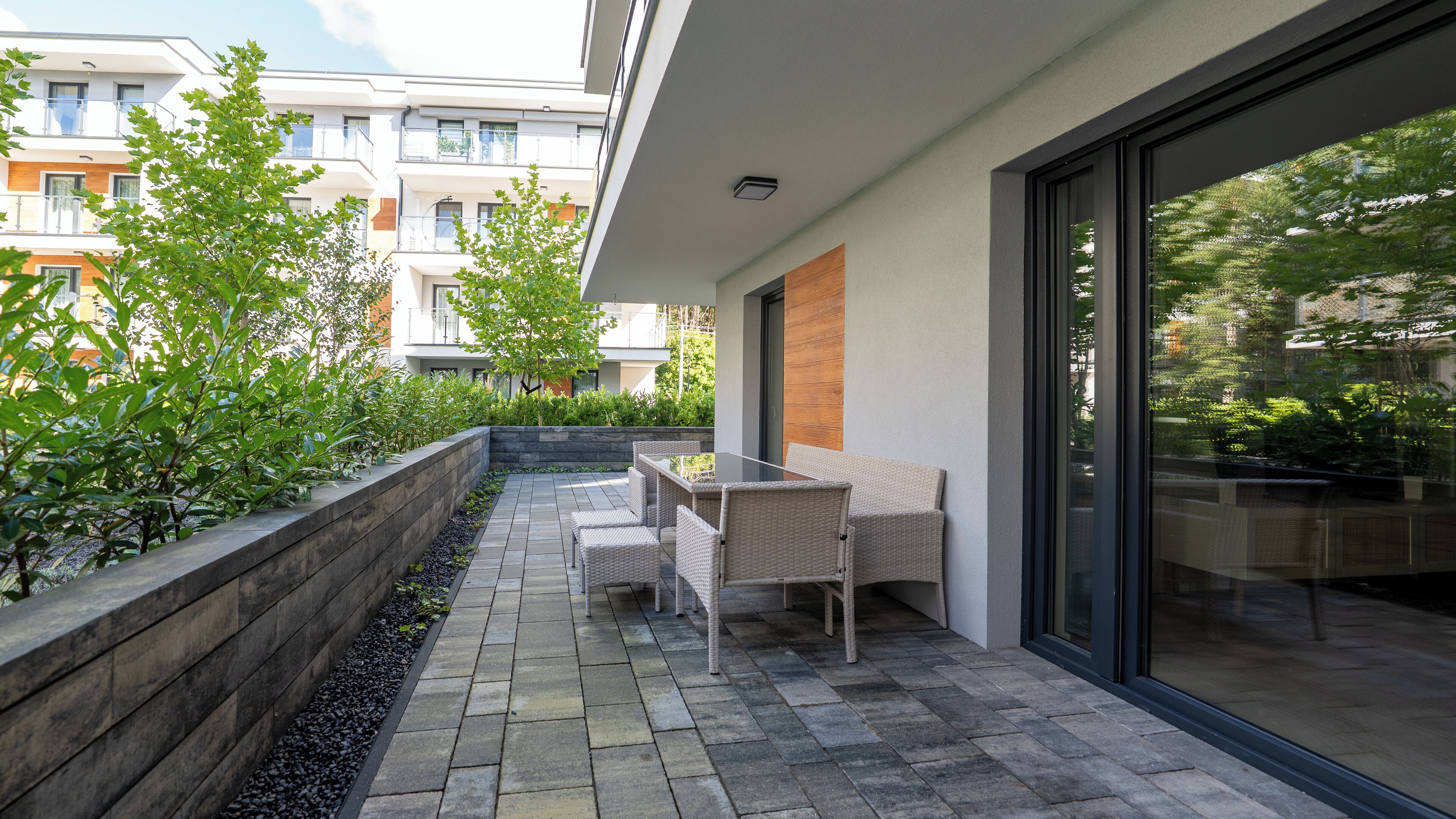 A modern outdoor patio with a seating area, a stone pathway, and a view of neighboring buildings.