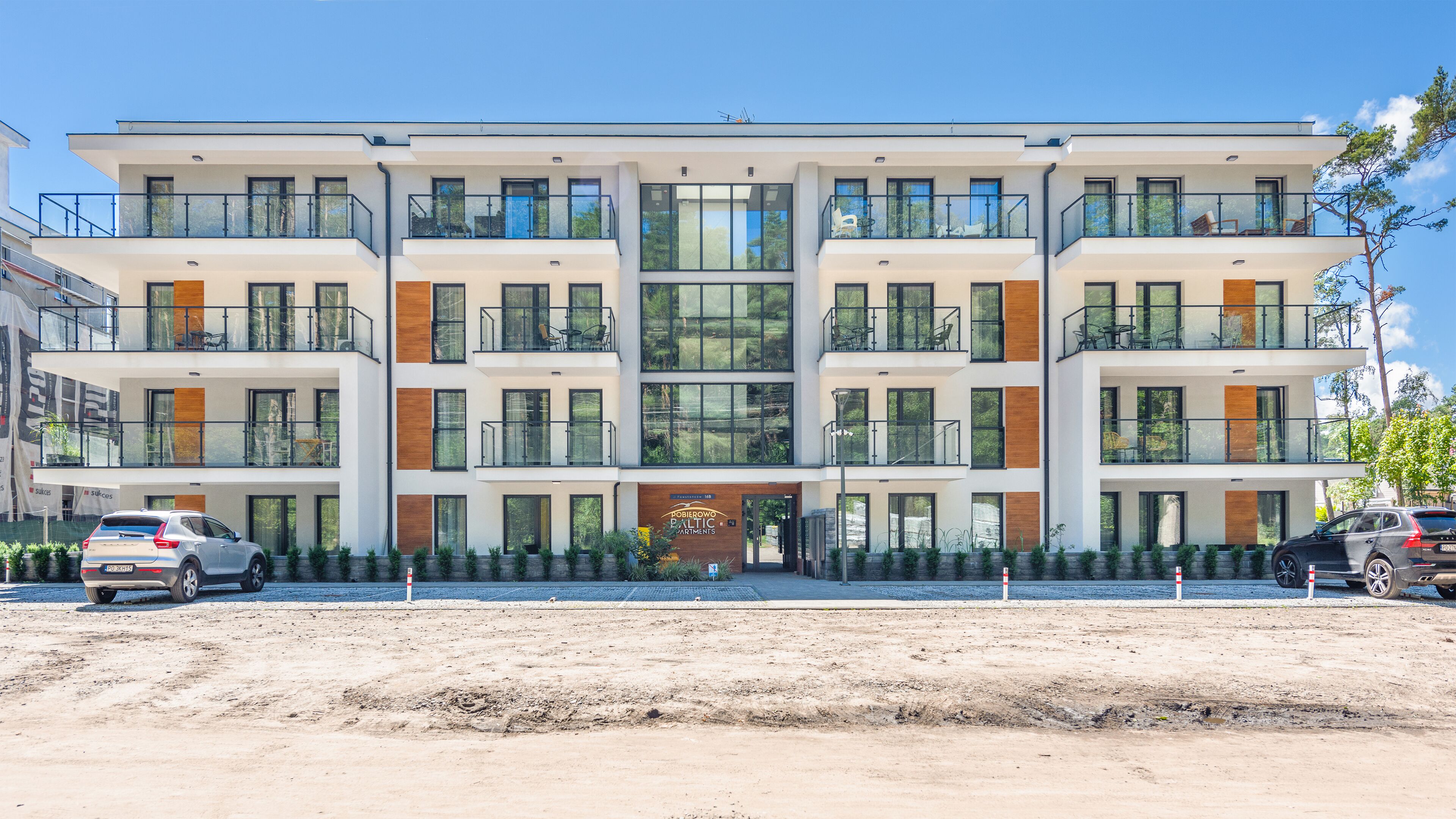 Un edificio de apartamentos de varios pisos con balcones, ventanas amplias y un cartel que indica 'Pobierowo Baltic Apartments'.