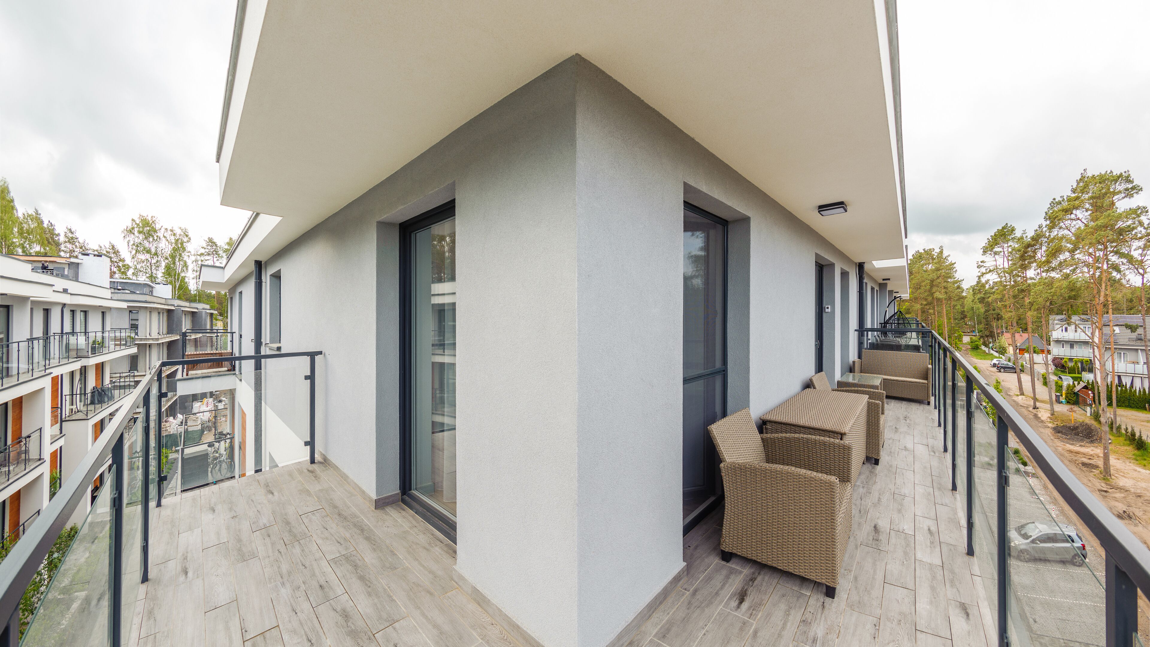 Un apartamento moderno con balcón, amueblado con mobiliario de mimbre y vistas a edificios y árboles cercanos.