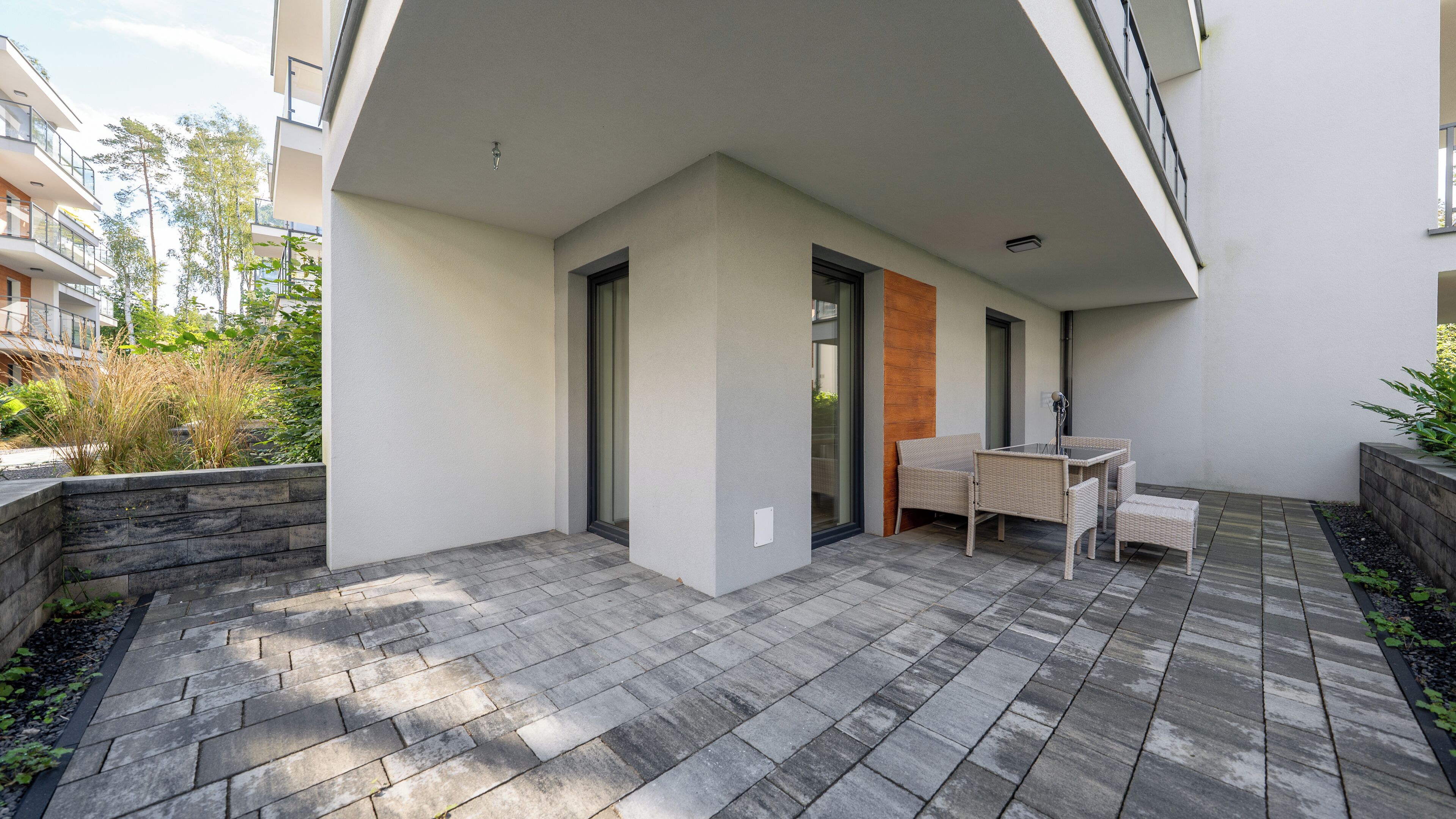 A modern outdoor patio area with a stone floor, a seating area with a table and chairs, and a glass door leading to a balcony.