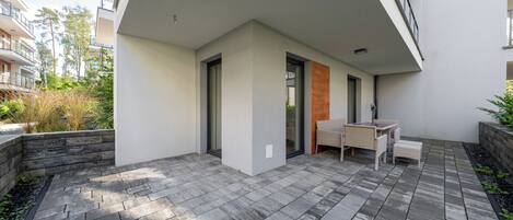A modern outdoor patio area with a stone floor, a seating area with a table and chairs, and a glass door leading to a balcony.
